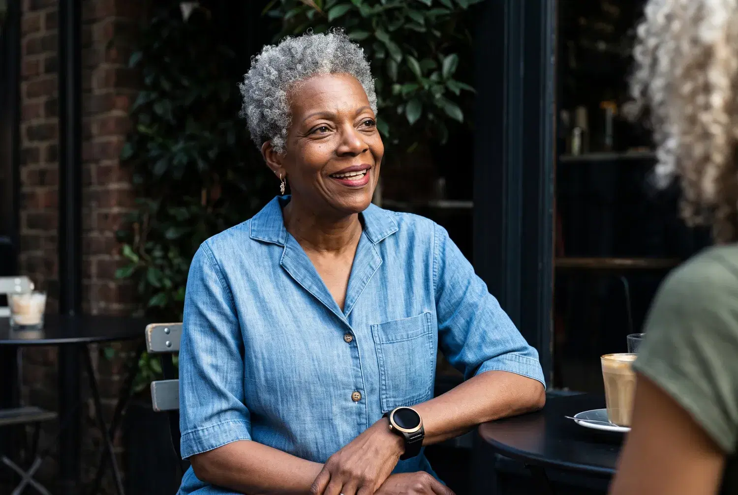 An older woman relaxes at a café table wearing her Kanega Watch